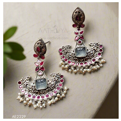 Ornate earrings with gemstones and pearls on a light background