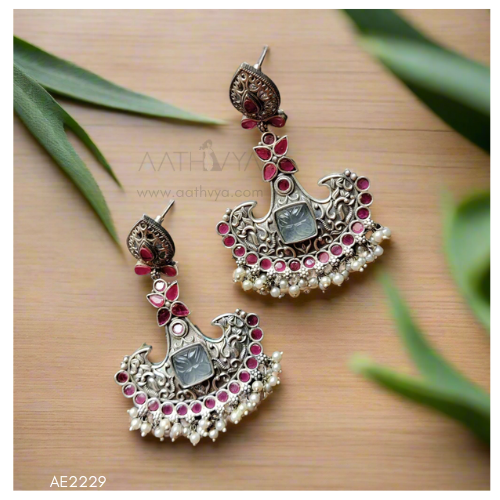 Ornate silver earrings with red stones on a wooden surface with green leaves.