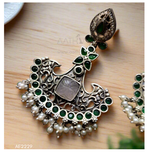 Ornate silver and green gemstone earring on a wooden surface