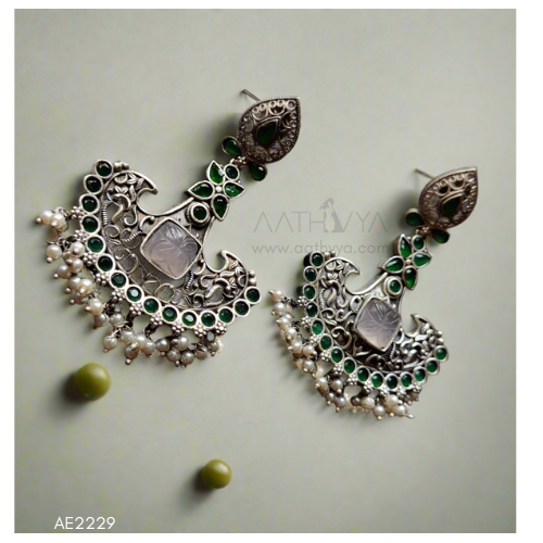 Ornate silver earrings with green stones and pearls on a light gray background
