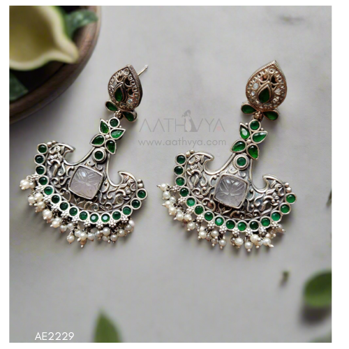 Ornate earrings with green and silver design on a light background