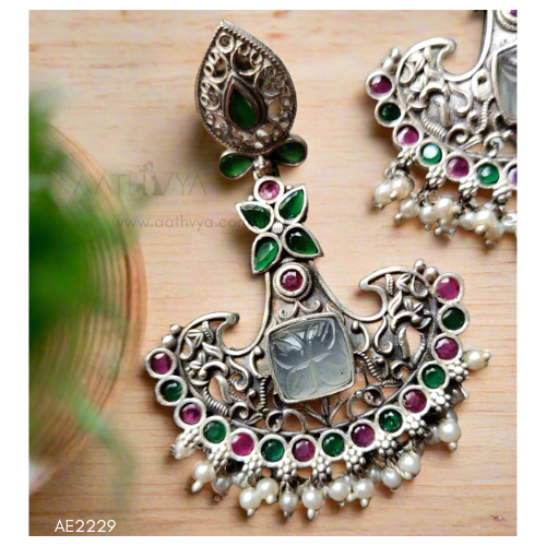 Ornate silver earrings with gemstones and pearls on a wooden surface