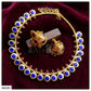 Gold-plated jewelry set featuring a necklace and matching earrings with round blue stones and small pink accent stones, displayed on a dark red velvet background.