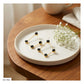 A pair of gold geometric triangle earrings with black circular studs, displayed on a round white ceramic plate on a wooden table next to baby's breath flowers.