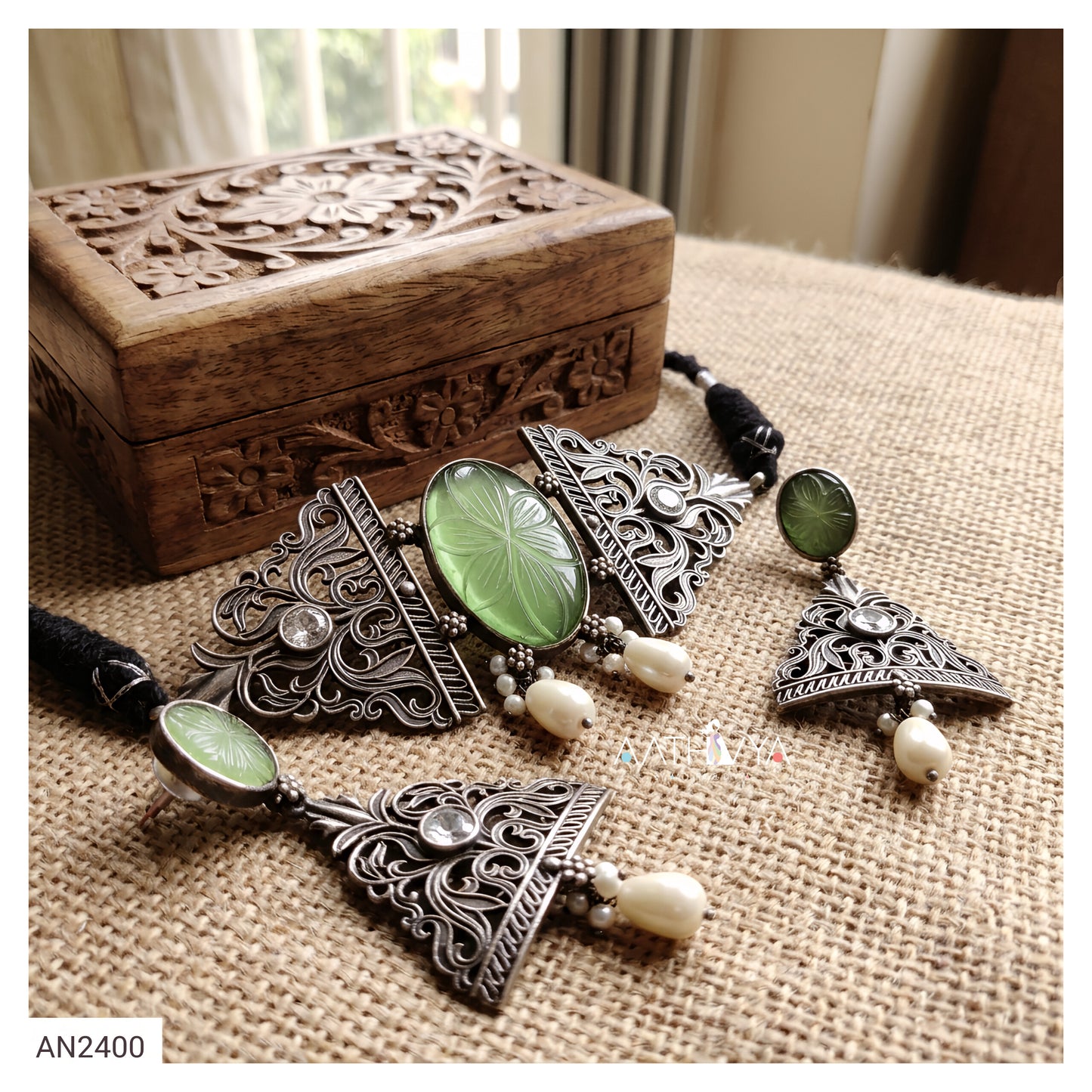 Silver-toned filigree jewelry set with green oval cabochon stones and white bead accents, displayed on a burlap surface beside a carved wooden box.