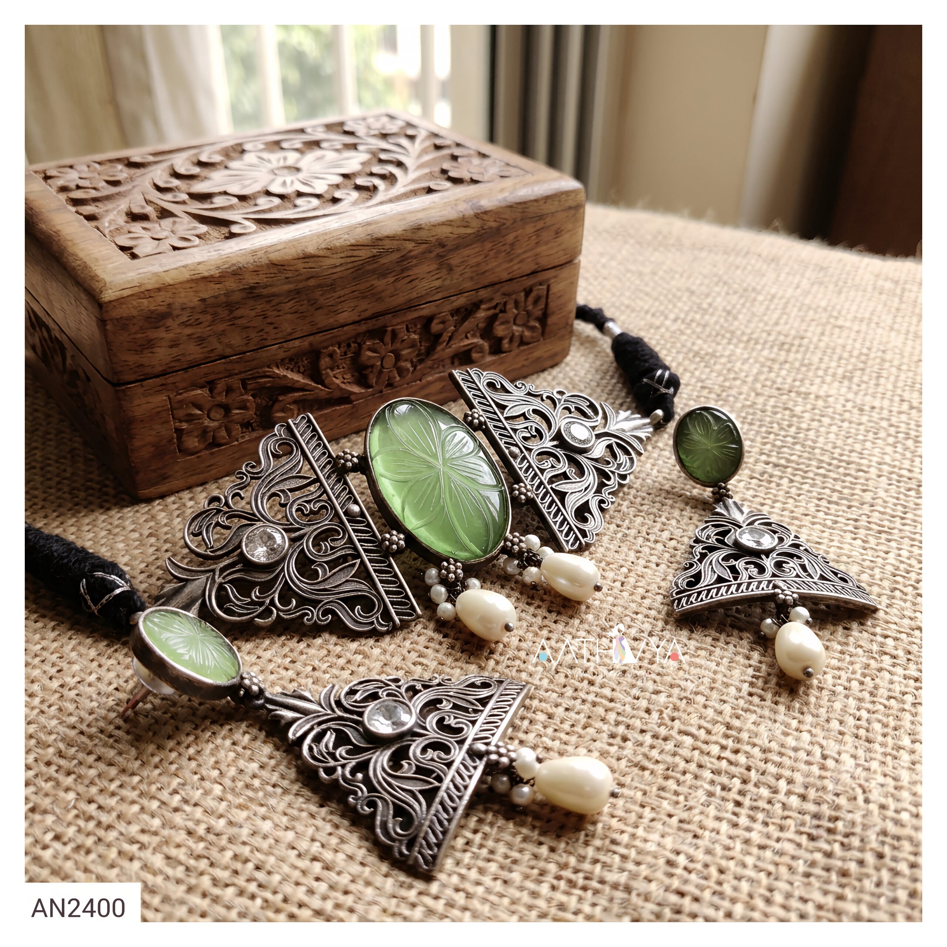 Silver-toned filigree jewelry set with green oval cabochon stones and white bead accents, displayed on a burlap surface beside a carved wooden box.