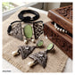 A jewelry set displayed on a beige burlap cloth next to a carved wooden box. The set includes a black braided bracelet, a silver-toned filigree necklace with oval green stone pendants and small white beads, matching silver-toned earrings, and a partial pearl necklace inside the wooden box.