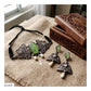 A jewelry set displayed on a burlap fabric surface next to a carved wooden box. The set includes a necklace with a black cord and three silver-toned filigree triangles with oval green stone centers, plus matching drop earrings with silver-toned filigree, green oval stones, and white bead drops.