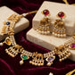 Gold-toned Indian jewelry set featuring a necklace and matching earrings with elephant motifs, pearl bead drops, and colorful gemstone accents, displayed on cream blocks over a dark red velvet background.