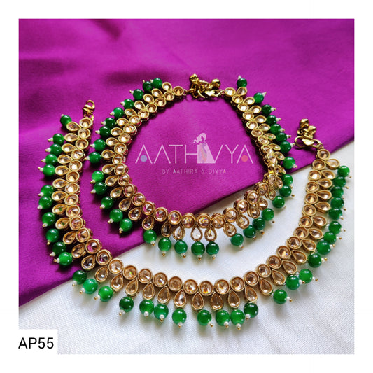 A pair of green and gold beaded AD anklets with mehndi plating, displayed on a purple surface.